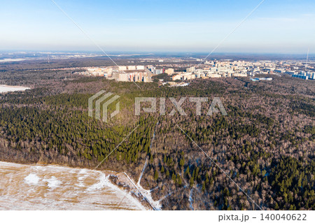Sprawling winter forest borders a distant city skyline. Green conifers mix with bare trees, contrasting urban development with nature's tranquil, snow-dusted landscape Sprawling winter forest borders a distant city skyline. Green conifers mix with bare trees, contrasting urban development with nature's tranquil, snow-dusted landscape 140040622