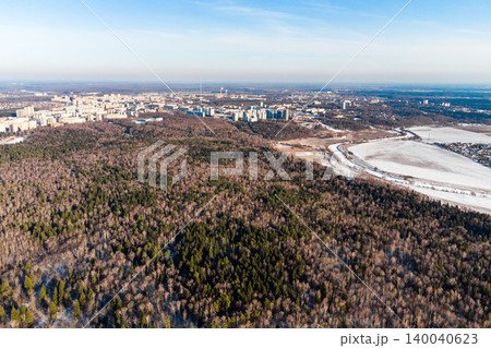 Aerial view of a vast wintry forest meeting a sprawling city under a clear sky, showcasing the transition from nature to urban development Aerial view of a vast wintry forest meeting a sprawling city under a clear sky, showcasing the transition from nature to urban development 140040623