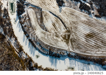 Winter aerial vista of a snaking, partially frozen river next to snow-dusted fields with intriguing tracks. Cold season's calm landscape 140040625