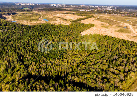 Expansive forest stretching towards a large open quarry pit with water bodies. Evidence of human impact on nature, urban sprawl in the distance 140040929