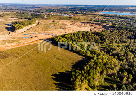 Aerial view of a vast open-pit quarry, showcasing raw earth and excavation. It borders lush forest and fields, illustrating industrial impact on the landscape 140040930