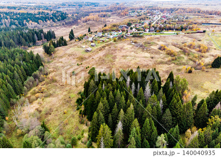 Expansive evergreen forest meets rural village perched on a hill, surrounded by golden autumn fields under an overcast sky. A serene, rustic landscape from above Expansive evergreen forest meets rural village perched on a hill, surrounded by golden autumn fields under an overcast sky. A serene, rustic landscape from above 140040935