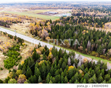 Aerial view of a highway cutting through a lush autumn forest. A mix of evergreens and golden deciduous trees dominate the scene, offering a vibrant natural display Aerial view of a highway cutting through a lush autumn forest. A mix of evergreens and golden deciduous trees dominate the scene, offering a vibrant natural display 140040940