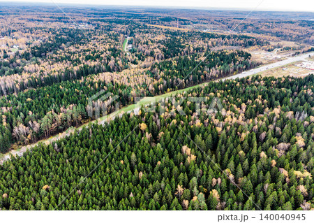 Aerial view of a vast autumn forest with a highway winding through, showcasing vibrant green conifers and hints of golden foliage 140040945
