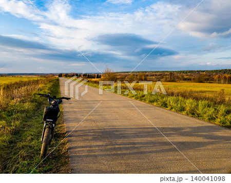 E-bike chilling roadside, golden fields under a vast sky. Perfect pause during a serene autumn ride E-bike chilling roadside, golden fields under a vast sky. Perfect pause during a serene autumn ride 140041098