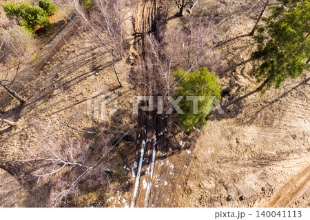 Rough dirt trail meandering through a sparse woodland with dry grass. Small snow patches punctuate the path, indicating late winter or early spring Rough dirt trail meandering through a sparse woodland with dry grass. Small snow patches punctuate the path, indicating late winter or early spring 140041113