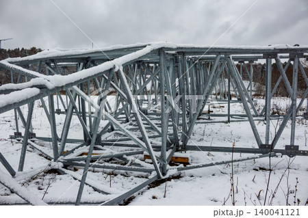 Galvanized steel lattice power pylon components on snowy ground, ready for assembly. Energy infrastructure construction during winter, awaiting erection Galvanized steel lattice power pylon components on snowy ground, ready for assembly. Energy infrastructure construction during winter, awaiting erection 140041121