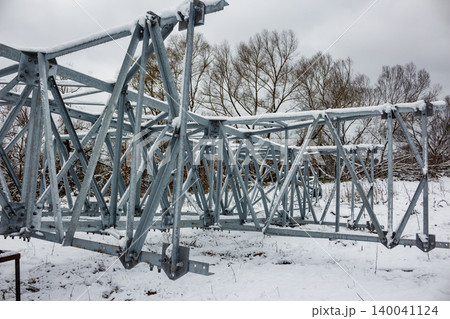 Heavy steel transmission tower sections covered in snow, resting on a wintry ground. Unassembled power pylon awaiting installation 140041124