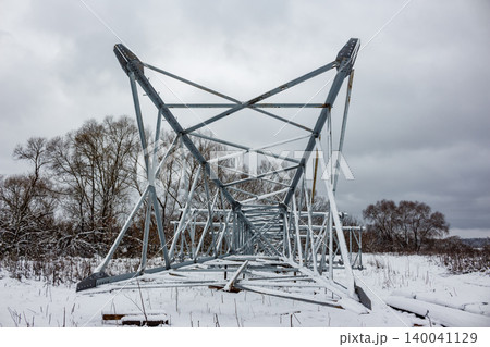 Galvanized steel lattice structure of an electric pylon laid out for installation in a cold, snowy landscape. Winter construction scene Galvanized steel lattice structure of an electric pylon laid out for installation in a cold, snowy landscape. Winter construction scene 140041129