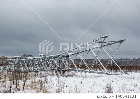 Massive power grid pylon framework rests in a snowy field, awaiting installation. Its robust metal structure, dusted with winter flakes, contrasts with the bleak sky Massive power grid pylon framework rests in a snowy field, awaiting installation. Its robust metal structure, dusted with winter flakes, contrasts with the bleak sky 140041131