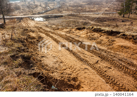 Sandy slope with prominent tire tracks leading downhill. The rugged terrain and dry, sparse vegetation suggest an off-road adventure or construction site 140041164