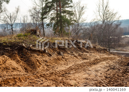 Textured sandy terrain in the foreground, deeply scored by tire tracks. A desolate landscape of bare trees and a hazy, distant horizon unfolds behind 140041169