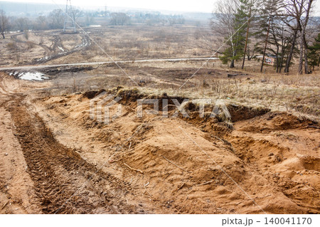 Uneven, reddish-brown slope with deep vehicle tracks and freshly disturbed earth in the foreground. A desolate, early spring landscape stretches behind Uneven, reddish-brown slope with deep vehicle tracks and freshly disturbed earth in the foreground. A desolate, early spring landscape stretches behind 140041170