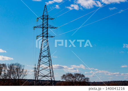 Towering power pylon stands proudly against a bright blue sky with wispy clouds. Its high-voltage lines deliver energy across a serene, bare landscape Towering power pylon stands proudly against a bright blue sky with wispy clouds. Its high-voltage lines deliver energy across a serene, bare landscape 140041216