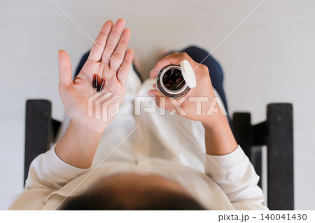 Hands hold pills and bottle against soft background. Person shows medication with calm, thoughtful gesture. Image conveys health, care, or wellness focus. Ideal for medical, lifestyle Hands hold pills and bottle against soft background. Person shows medication with calm, thoughtful gesture. Image conveys health, care, or wellness focus. Ideal for medical, lifestyle 140041430