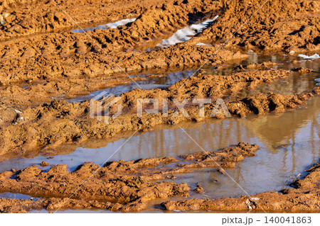 Deep tire tracks carved into thick wet clay soil creating a muddy and messy off-road trail filled with stagnant rainwater puddles after heavy spring rains Deep tire tracks carved into thick wet clay soil creating a muddy and messy off-road trail filled with stagnant rainwater puddles after heavy spring rains 140041863