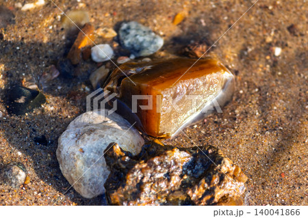 Sun-kissed chalcedony and quartz river pebbles glisten in shallow sandy water. Nature's subtle beauty in radiant detail Sun-kissed chalcedony and quartz river pebbles glisten in shallow sandy water. Nature's subtle beauty in radiant detail 140041866