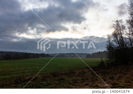 Dramatic November sky over a vast green meadow at the edge of a forest, showing cold autumn vibes with heavy clouds and soft light filtering through the gloomy atmosphere Dramatic November sky over a vast green meadow at the edge of a forest, showing cold autumn vibes with heavy clouds and soft light filtering through the gloomy atmosphere 140041874