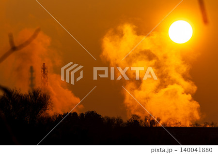 Golden winter sunset drenches colossal industrial steam plume. Towering chimney casts shadow on bright vapor, vivid orange sky backdrop Golden winter sunset drenches colossal industrial steam plume. Towering chimney casts shadow on bright vapor, vivid orange sky backdrop 140041880