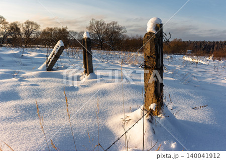 Broken concrete posts and rusty barbed wire stand in a bright, sunlit snowy field, suggesting old boundaries and wintry open space Broken concrete posts and rusty barbed wire stand in a bright, sunlit snowy field, suggesting old boundaries and wintry open space 140041912