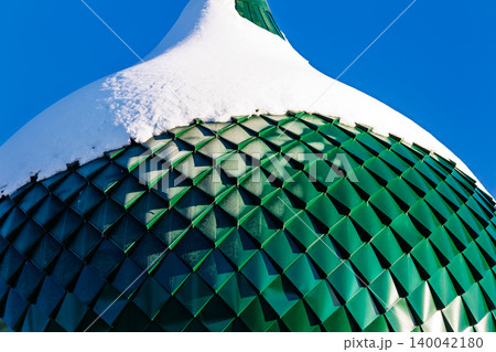 Stunning close-up of a Russian Orthodox church's onion dome, its emerald scales blanketed by crisp white snow under a brilliant azure sky 140042180