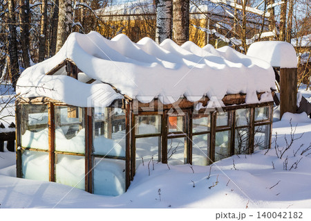 Rustic wooden greenhouse heavily blanketed in pristine, wavy snow under a bright winter sun. Tranquil dormant garden scene Rustic wooden greenhouse heavily blanketed in pristine, wavy snow under a bright winter sun. Tranquil dormant garden scene 140042182