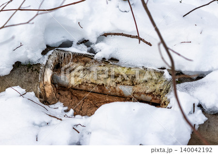 Exposed, tattered thermal insulation on a frozen outdoor pipe, buried in crisp winter snow, showing utility damage Exposed, tattered thermal insulation on a frozen outdoor pipe, buried in crisp winter snow, showing utility damage 140042192