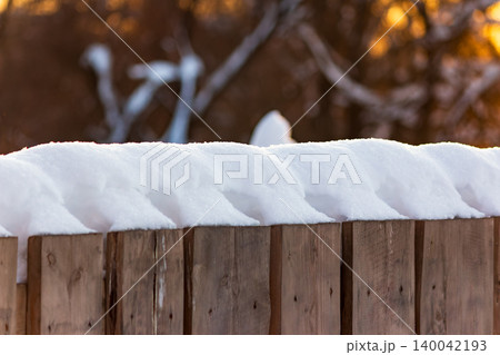 Soft, pristine snow perfectly caps a weathered wood fence, illuminated by subtle golden light. Tranquil winter scene with a cozy blurred background Soft, pristine snow perfectly caps a weathered wood fence, illuminated by subtle golden light. Tranquil winter scene with a cozy blurred background 140042193