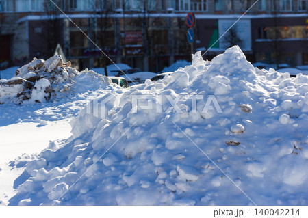 Piles of snow on city streets, cleared from roads and sidewalks, create abstract winter sculptures against a blurred urban background Piles of snow on city streets, cleared from roads and sidewalks, create abstract winter sculptures against a blurred urban background 140042214