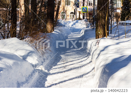Sunny winter path, deeply carved through pristine snowdrifts, bordered by skeletal trees. A tranquil scene for peaceful seasonal walks and serene landscapes 140042223