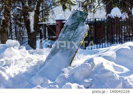 A splintered green board emerges from a thick pile of snow, likely a result of tractor snow removal. Bright winter sunlight illuminates the scene A splintered green board emerges from a thick pile of snow, likely a result of tractor snow removal. Bright winter sunlight illuminates the scene 140042226