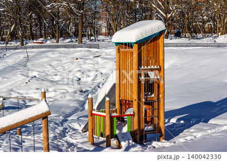 Empty wooden playground structure blanketed in fresh snow under a crisp winter sun. Perfect for seasonal themes or childhood nostalgia Empty wooden playground structure blanketed in fresh snow under a crisp winter sun. Perfect for seasonal themes or childhood nostalgia 140042330