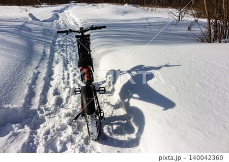 Rugged electric fatbike on a pristine snow trail, its long shadow hinting at winter adventures. Sunny frosty day, extreme e-biking journey Rugged electric fatbike on a pristine snow trail, its long shadow hinting at winter adventures. Sunny frosty day, extreme e-biking journey 140042360