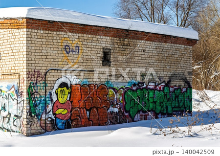 Bold, colorful graffiti on a derelict brick wall set against a crisp, snowy winter landscape under bright sun 140042509