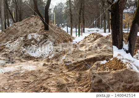 Huge piles of dirty, melting snow and sand mixed together after winter road clearing, revealing muddy ground texture 140042514