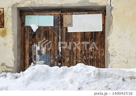 Rustic wooden garage doors partially buried under a thick mound of dirty winter snow and ice Rustic wooden garage doors partially buried under a thick mound of dirty winter snow and ice 140042516