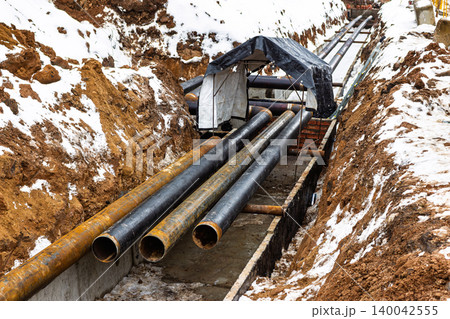 Heavy-duty pipes laid in a snowy trench during utility infrastructure development for new housing projects 140042555