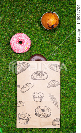 Freshly baked donuts and crumpled paper bag on a grass background .Top view. 140042704
