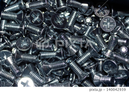 Close-up of numerous shiny galvanized DIN 965 screws, a jumbled pile of threaded fasteners with countersunk heads. Essential hardware for construction and assembly projects Close-up of numerous shiny galvanized DIN 965 screws, a jumbled pile of threaded fasteners with countersunk heads. Essential hardware for construction and assembly projects 140042939