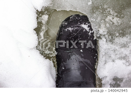 Heavy boot sinking into treacherous, melting river ice. A stark warning of thin ice danger in late winter and fragile surfaces Heavy boot sinking into treacherous, melting river ice. A stark warning of thin ice danger in late winter and fragile surfaces 140042945