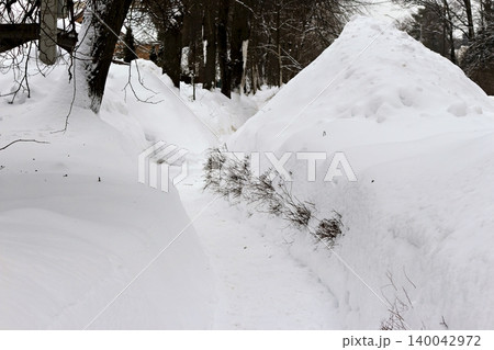 Towering white snowdrifts line a snug, cleared path, showcasing the pristine beauty of a tranquil winter landscape. Fresh snowfall creates a serene scene 140042972