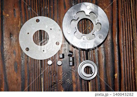 Disassembled electric bike motor freewheel clutch components, including metal rollers, small springs, and steel discs cleaned of old grease, arranged on a textured rustic wooden tabletop 140043282