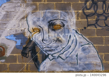 Nighttime alleyway features eerie painted image with haunting expression and vibrant spray paint accents Nighttime alleyway features eerie painted image with haunting expression and vibrant spray paint accents 140043296