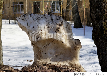 Dirty heap of old snow piled on a roadside, slowly melting under the bright spring sun in a city, showcasing textures of ice and debris amidst the seasonal thaw Dirty heap of old snow piled on a roadside, slowly melting under the bright spring sun in a city, showcasing textures of ice and debris amidst the seasonal thaw 140043307
