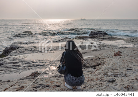 海辺の岩場で静かに海を見つめる女性の後ろ姿 海辺の岩場で静かに海を見つめる女性の後ろ姿 140043441