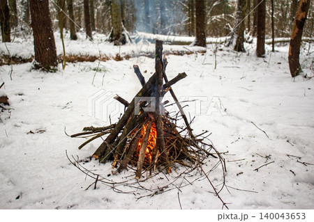 A cozy bonfire blazes warmly in a serene, snow-covered forest, its orange glow fighting the winter chill. Perfect for cold season adventures A cozy bonfire blazes warmly in a serene, snow-covered forest, its orange glow fighting the winter chill. Perfect for cold season adventures 140043653