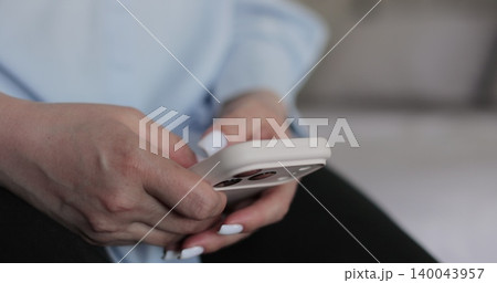 Close-up of hands of woman writes a text message on smartphone in the living room at home. Online shopping in social media. Close-up of hands of woman writes a text message on smartphone in the living room at home. Online shopping in social media. 140043957