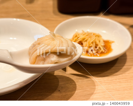 スプーンに乗せた小籠包。小籠包に乗せて食べる生姜黒酢のお皿。 140043959