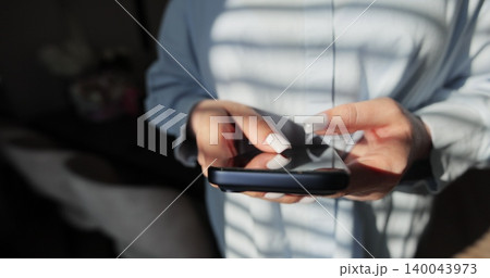 Close-up of hands of woman writes a text message on smartphone in the living room at home. Online shopping in social media. Close-up of hands of woman writes a text message on smartphone in the living room at home. Online shopping in social media. 140043973