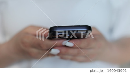 Hand of girl using smartphone in the living room at home, typing message. Close-up of young women hand. 140043991
